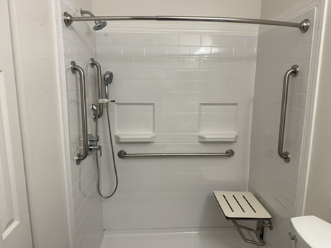 The same bathroom converted to a curbless walk-in shower with grab bars and a folding bench